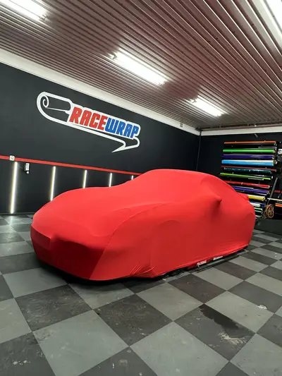 Auto pod czerwonym pokrowcem CarCapes w studiu oklejania
