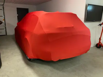 Auto pod czerwonym pokrowcem CarCapes w garażu przy domu