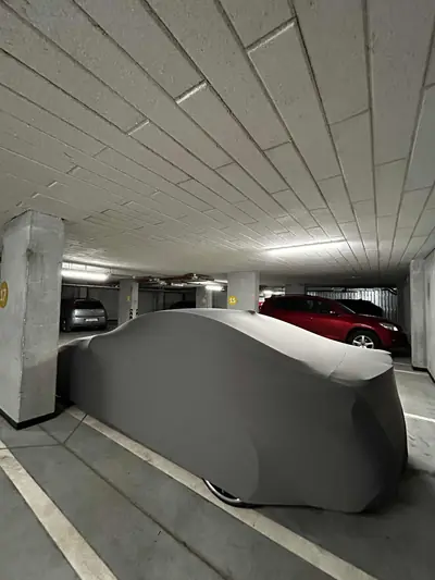 Auto pod szarym pokrowcem CarCapes na parkingu podziemnym