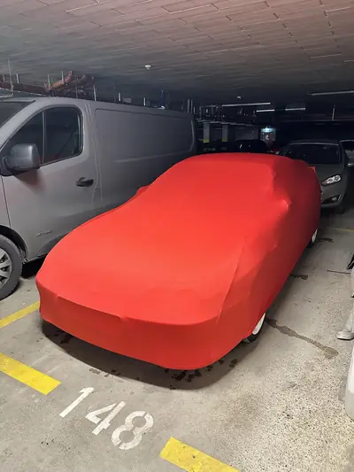 Auto pod czerwonym pokrowcem CarCapes na miejscu parkingowym