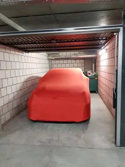 Auto pod czerwonym pokrowcem CarCapes w wąskim boksie garażowym