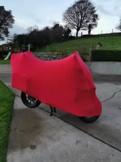 Motocykl pod czerwonym pokrowcem CarCapes przed domem