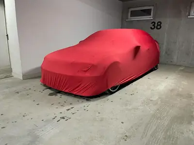 Auto pod czerwonym pokrowcem CarCapes w garażu